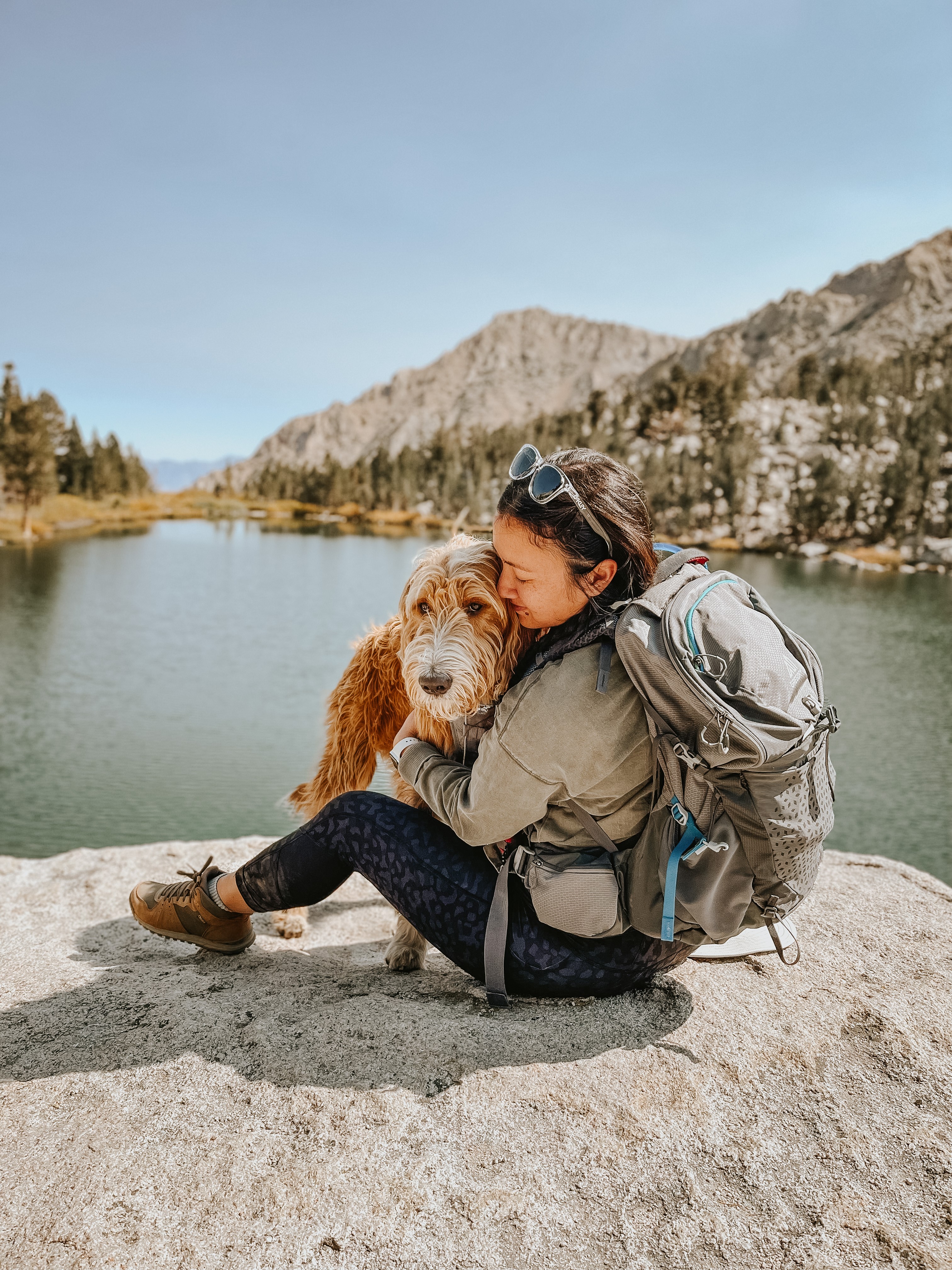 Julianna hugs Rado, a tan and white labradoodle, as they sit on a rock overlooking Flower Lake.